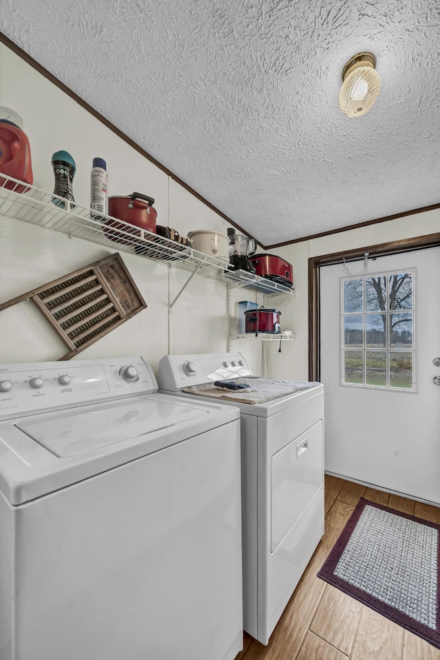 clothes washing area with light wood-type flooring, ornamental molding, a textured ceiling, and washing machine and clothes dryer