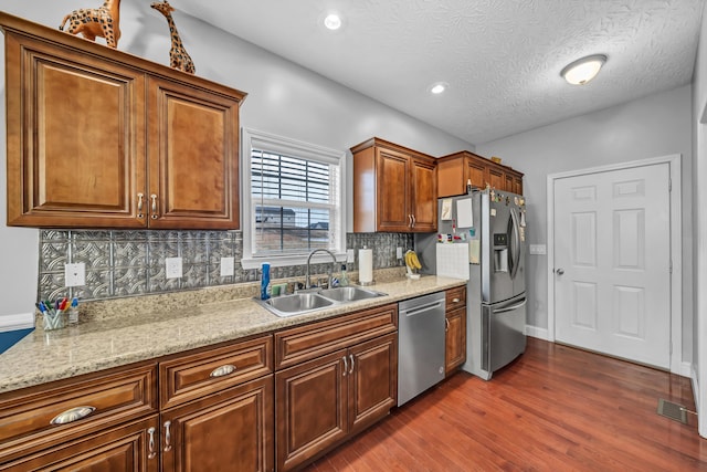 kitchen with sink, dark hardwood / wood-style floors, a textured ceiling, appliances with stainless steel finishes, and light stone counters