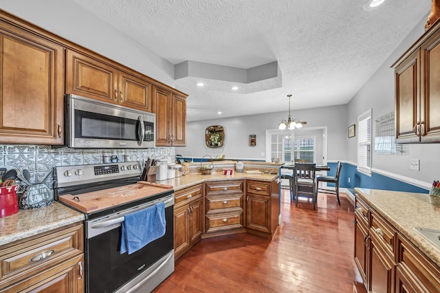 kitchen with appliances with stainless steel finishes, backsplash, light stone counters, decorative light fixtures, and a notable chandelier