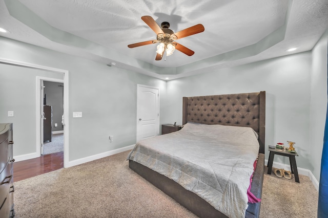 carpeted bedroom with a tray ceiling, ceiling fan, and a textured ceiling