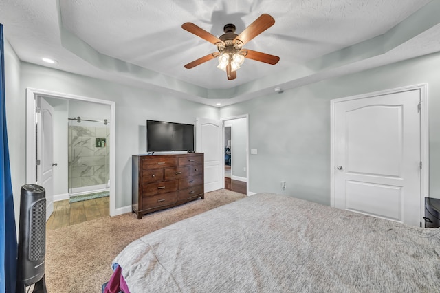 bedroom featuring ceiling fan, a raised ceiling, a textured ceiling, and connected bathroom