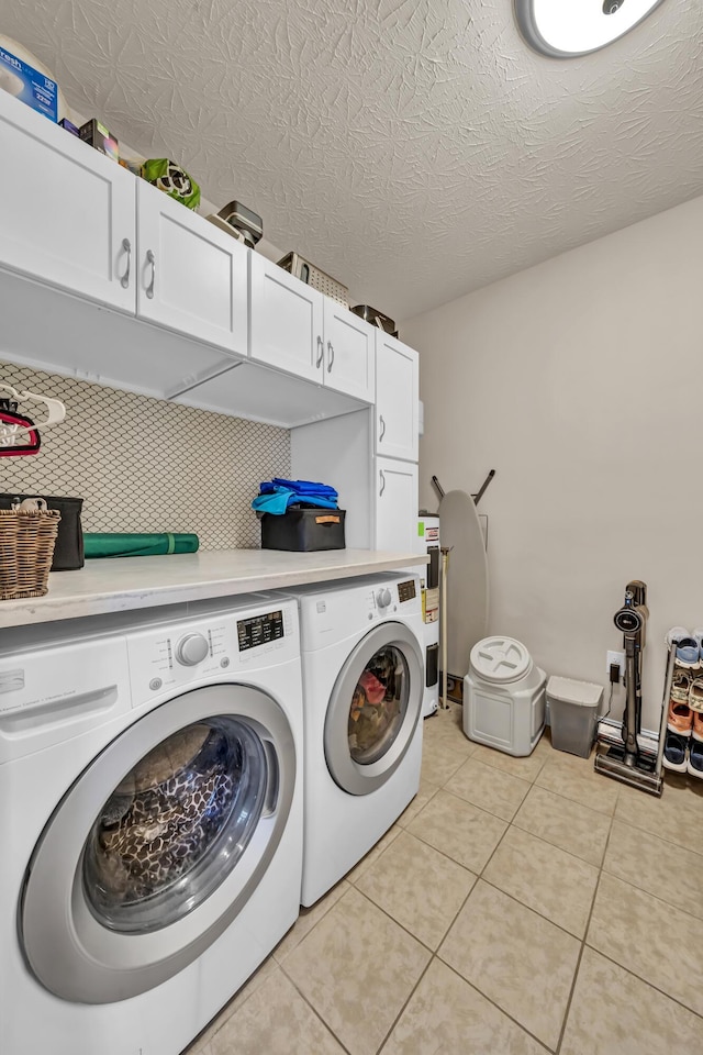 washroom featuring washing machine and clothes dryer, light tile patterned flooring, cabinets, and a textured ceiling