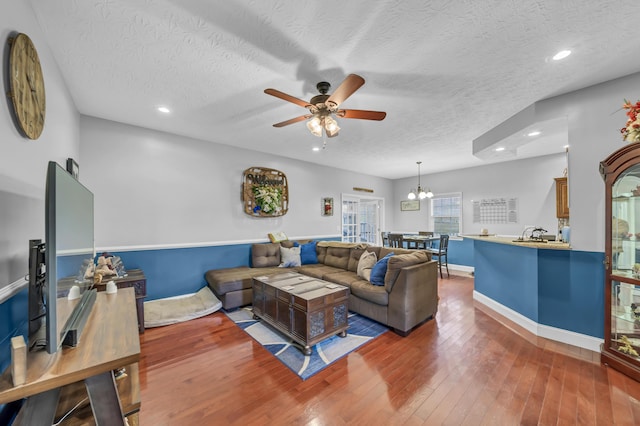 living room with ceiling fan with notable chandelier, hardwood / wood-style floors, a textured ceiling, and sink