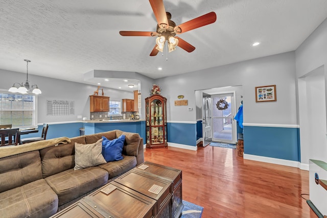 living room featuring a textured ceiling, light hardwood / wood-style floors, and ceiling fan with notable chandelier