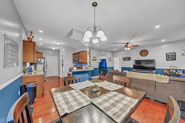 dining room featuring a textured ceiling, sink, light hardwood / wood-style floors, and ceiling fan with notable chandelier