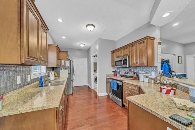 kitchen with sink, decorative backsplash, a textured ceiling, stainless steel appliances, and washer / clothes dryer