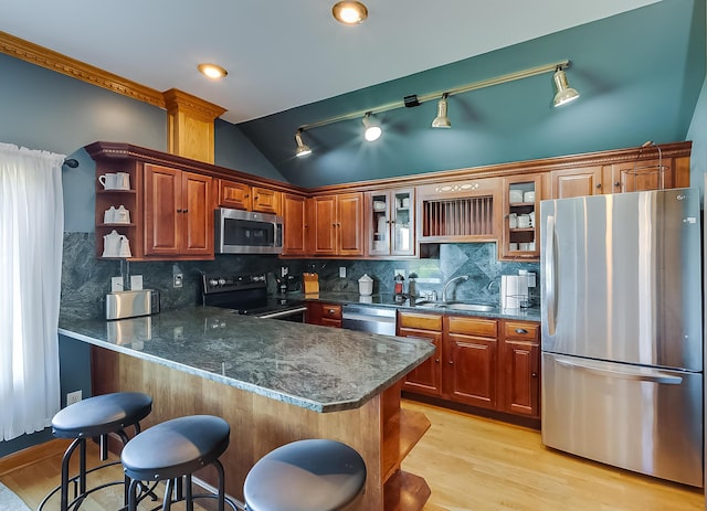 kitchen featuring sink, vaulted ceiling, appliances with stainless steel finishes, tasteful backsplash, and kitchen peninsula