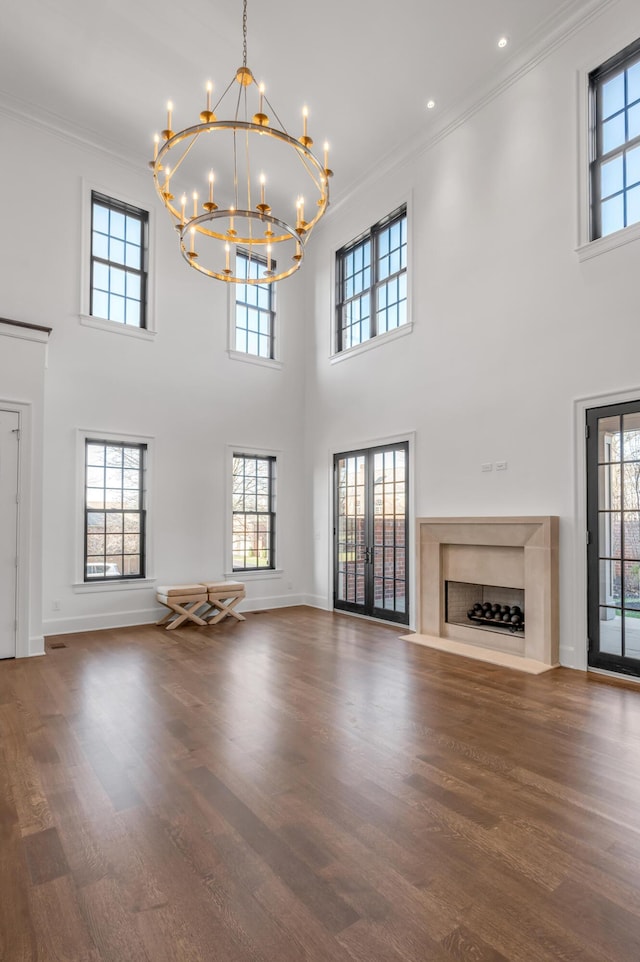 unfurnished living room featuring a fireplace, a towering ceiling, ornamental molding, and a notable chandelier