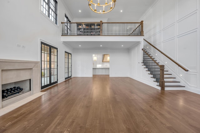 unfurnished living room featuring crown molding, an inviting chandelier, a high ceiling, and hardwood / wood-style flooring