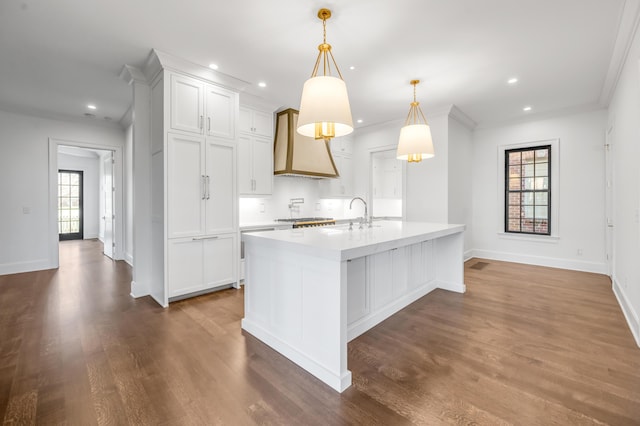 kitchen with dark hardwood / wood-style floors, an island with sink, custom range hood, decorative light fixtures, and white cabinetry