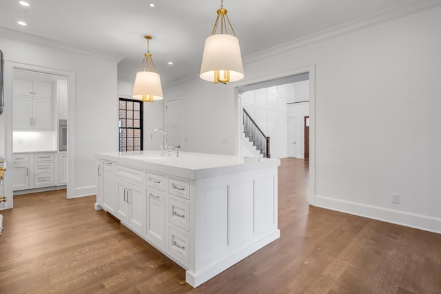 kitchen with pendant lighting, a kitchen island with sink, white cabinets, oven, and sink