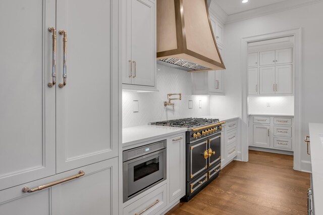 kitchen featuring decorative backsplash, wall chimney exhaust hood, range with two ovens, dark hardwood / wood-style floors, and white cabinetry