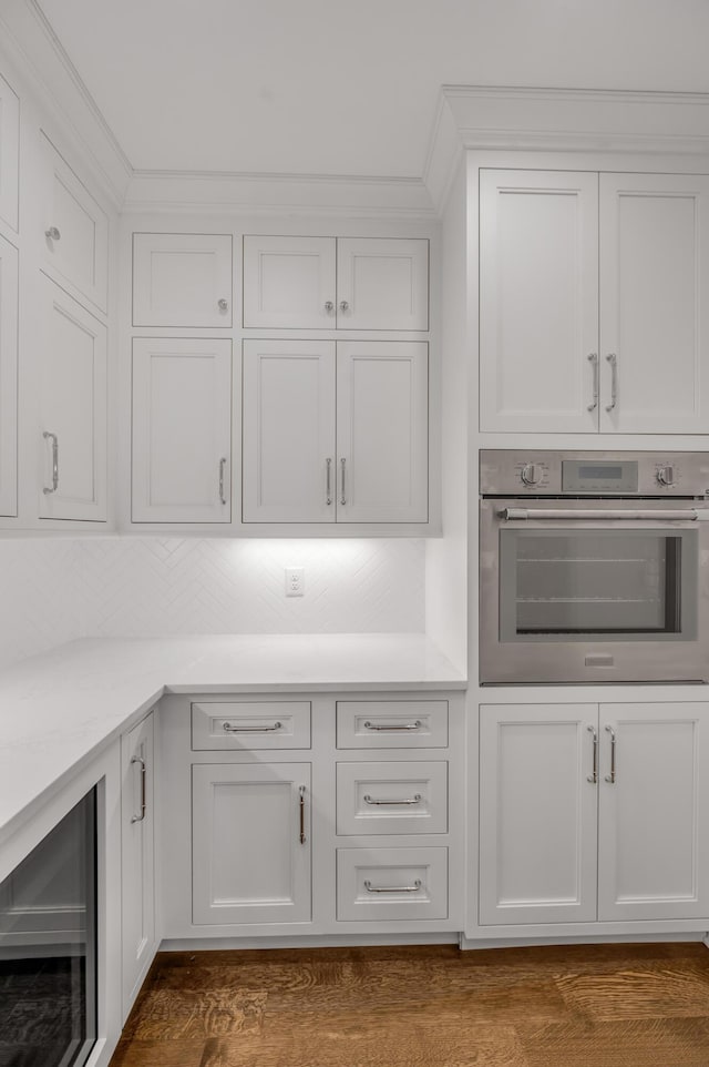 kitchen with dark wood-type flooring, oven, tasteful backsplash, white cabinetry, and beverage cooler