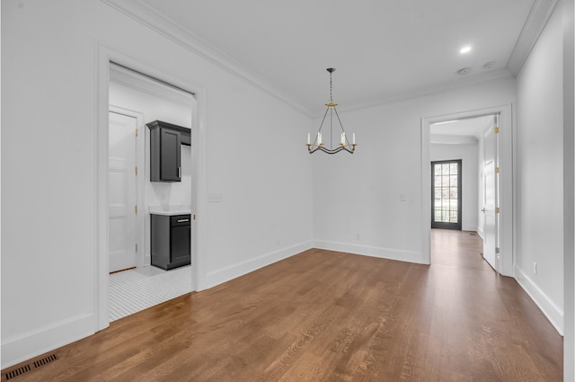 empty room with a chandelier, hardwood / wood-style floors, and ornamental molding