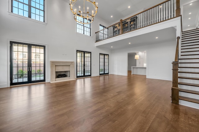 unfurnished living room with french doors, a chandelier, a high ceiling, and hardwood / wood-style flooring