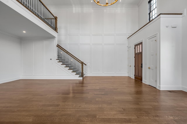 foyer entrance with a chandelier, a towering ceiling, ornamental molding, and dark wood-type flooring