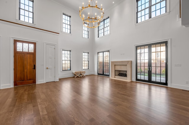 unfurnished living room with a high ceiling, an inviting chandelier, french doors, and crown molding