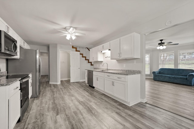 kitchen with sink, light stone counters, light hardwood / wood-style flooring, white cabinets, and appliances with stainless steel finishes