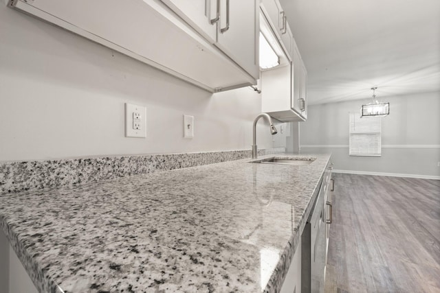 kitchen with decorative light fixtures, white cabinetry, light stone counters, and sink