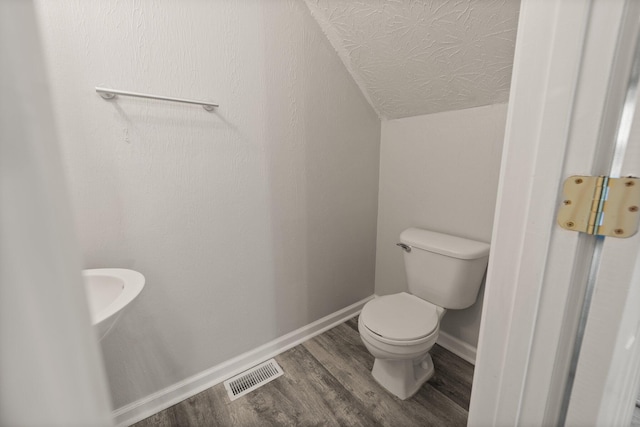 bathroom with a textured ceiling, wood-type flooring, lofted ceiling, and toilet