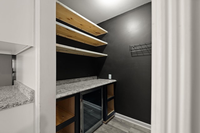 bar featuring light stone counters, wine cooler, and light hardwood / wood-style flooring