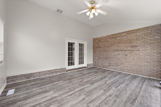 empty room with ceiling fan, brick wall, lofted ceiling, and wood-type flooring