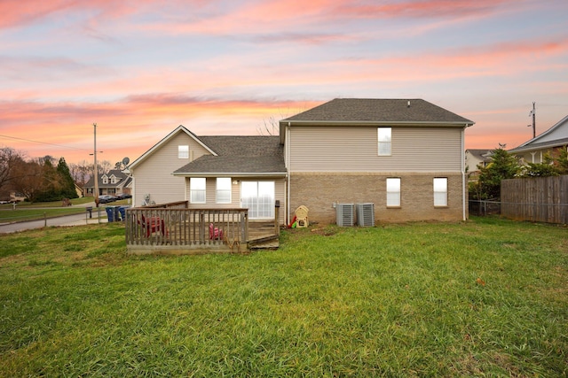 back house at dusk featuring central air condition unit, a lawn, and a wooden deck