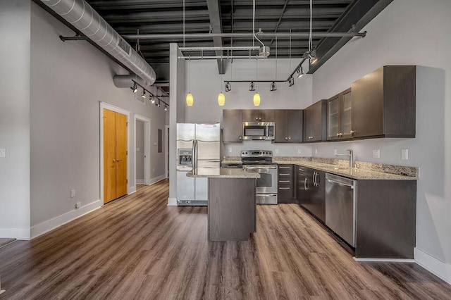 kitchen featuring light stone countertops, appliances with stainless steel finishes, a towering ceiling, and a kitchen island