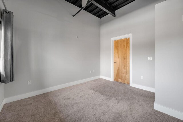 carpeted empty room featuring beam ceiling and a towering ceiling