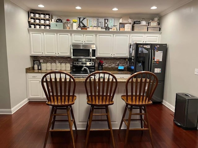 kitchen featuring white cabinetry, stainless steel appliances, backsplash, and dark stone countertops