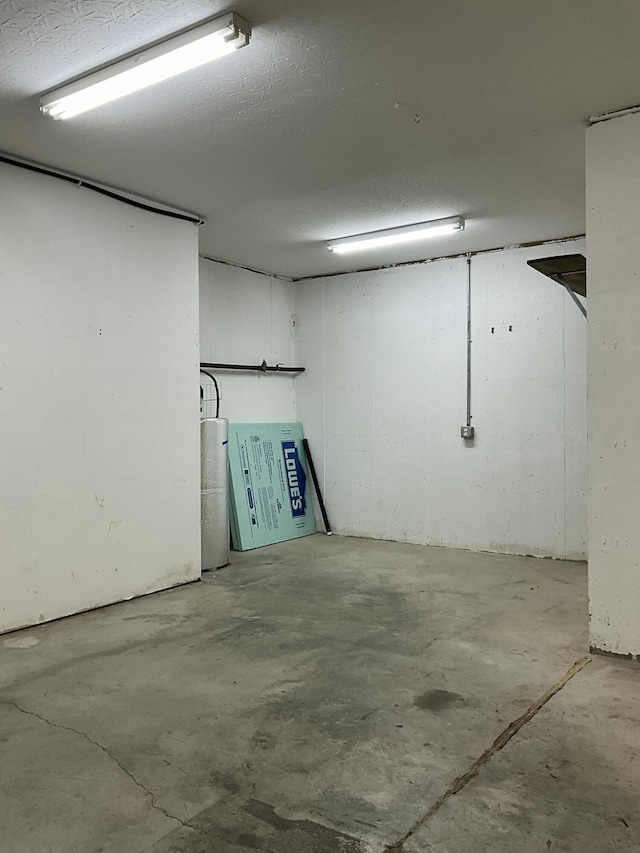 basement featuring water heater and a textured ceiling