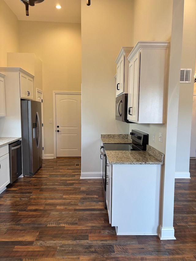 kitchen with white cabinetry, light stone counters, dark wood-type flooring, and appliances with stainless steel finishes