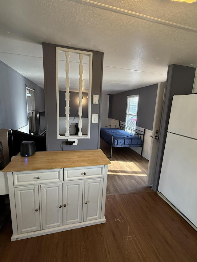 kitchen featuring white refrigerator, a textured ceiling, butcher block countertops, dark hardwood / wood-style flooring, and white cabinetry