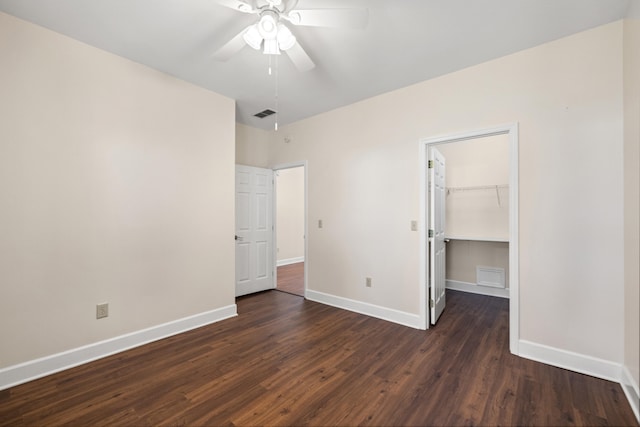 unfurnished bedroom with ceiling fan, a spacious closet, dark wood-type flooring, and a closet