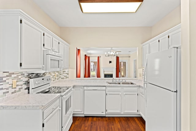 kitchen with backsplash, white appliances, sink, a notable chandelier, and white cabinetry