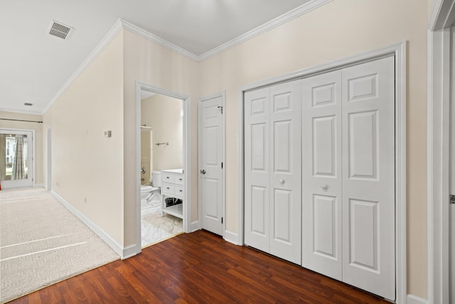 unfurnished bedroom with a closet, dark hardwood / wood-style flooring, ornamental molding, and ensuite bath