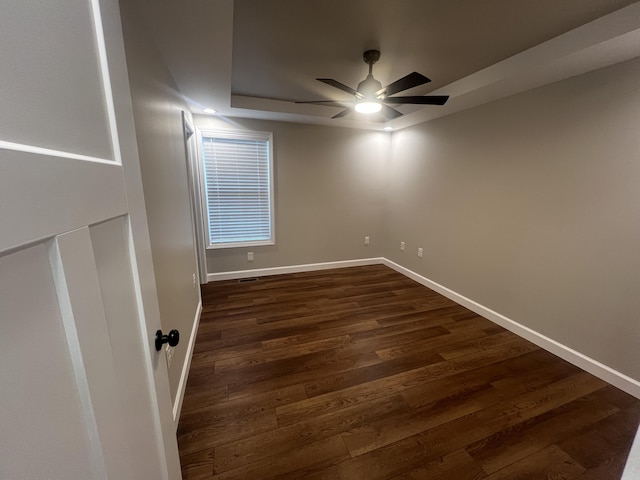 unfurnished room with a raised ceiling, ceiling fan, and dark wood-type flooring