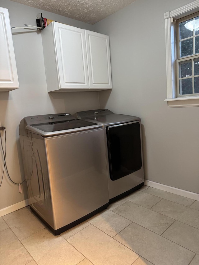 laundry room featuring cabinets, light tile patterned floors, washing machine and dryer, and a textured ceiling