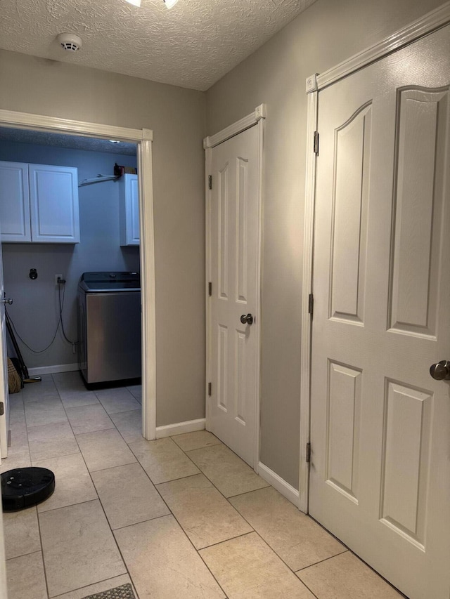 hallway with light tile patterned floors, a textured ceiling, and washer / dryer