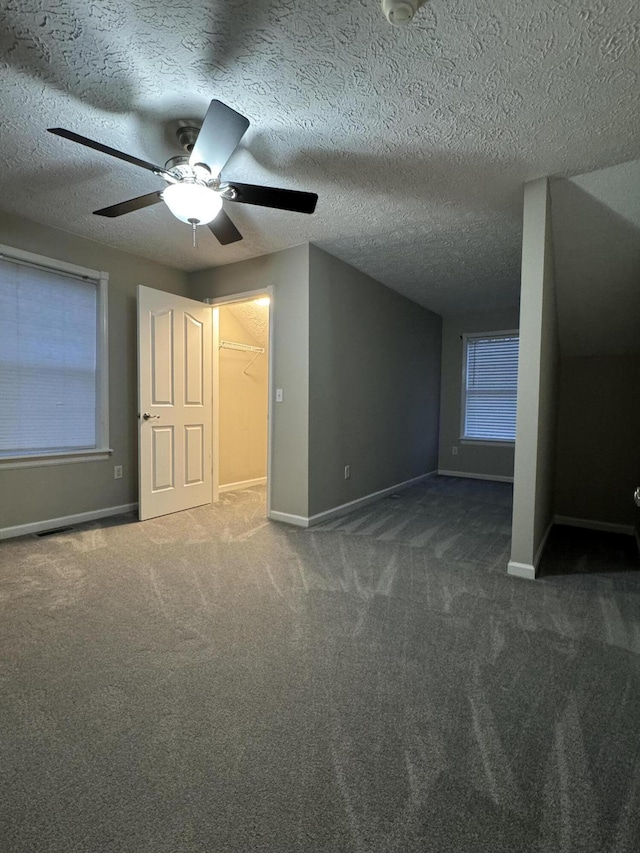 additional living space featuring dark colored carpet, ceiling fan, and a textured ceiling