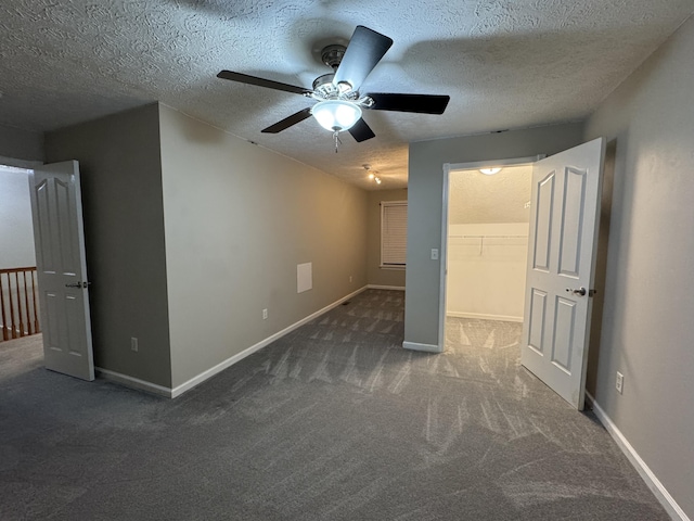 unfurnished bedroom featuring dark carpet, a walk in closet, ceiling fan, a textured ceiling, and a closet