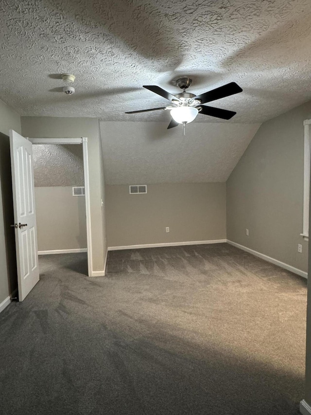 additional living space with dark carpet, lofted ceiling, and a textured ceiling