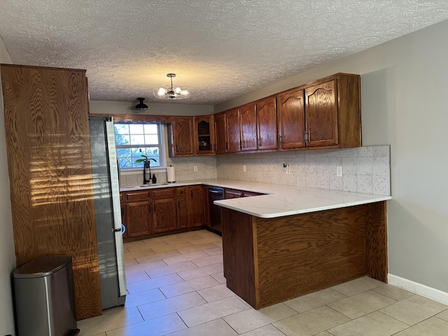 kitchen with dishwasher, hanging light fixtures, sink, kitchen peninsula, and stainless steel refrigerator