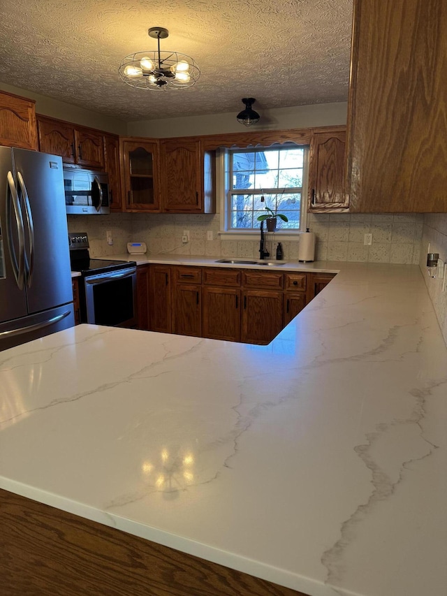 kitchen featuring backsplash, sink, a textured ceiling, stainless steel appliances, and a chandelier