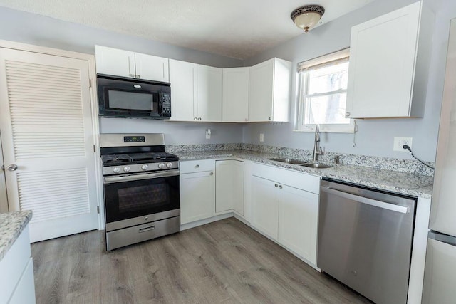 kitchen with sink, light wood-type flooring, light stone counters, white cabinetry, and stainless steel appliances