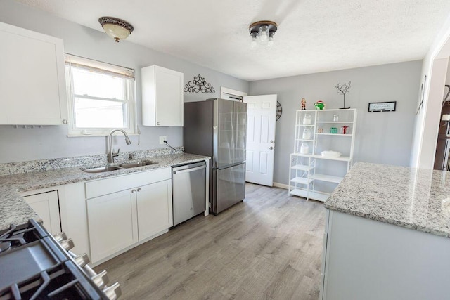 kitchen featuring light stone countertops, stainless steel appliances, white cabinetry, and sink