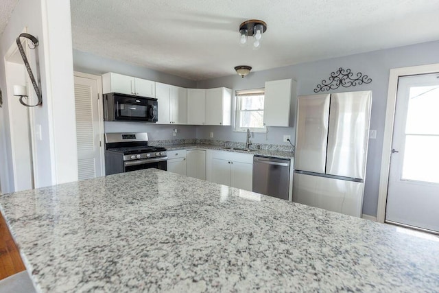 kitchen featuring appliances with stainless steel finishes, light stone counters, a textured ceiling, sink, and white cabinets