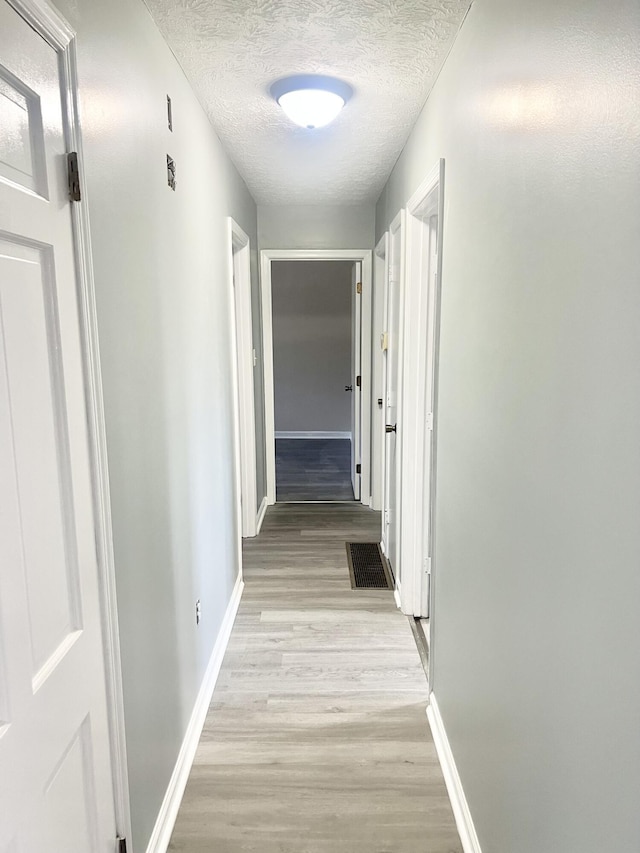 hall with light hardwood / wood-style floors and a textured ceiling