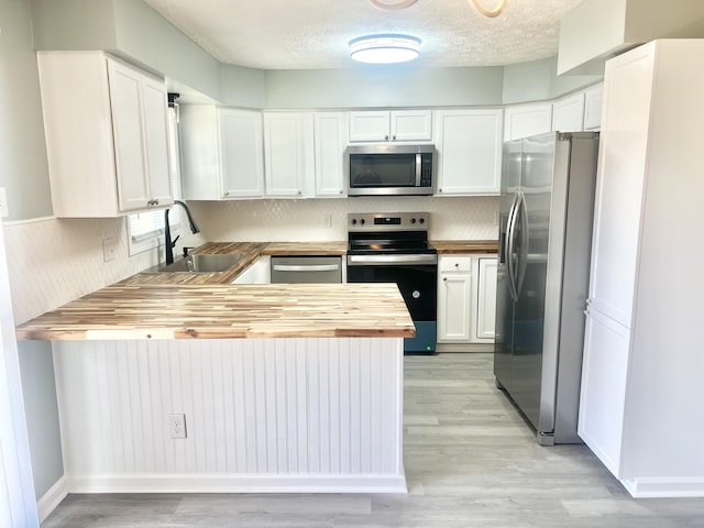 kitchen with wooden counters, appliances with stainless steel finishes, decorative backsplash, sink, and white cabinetry