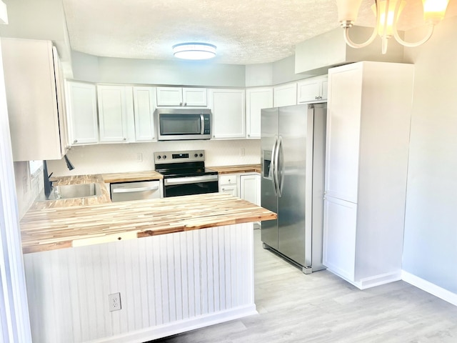 kitchen with wood counters, a textured ceiling, appliances with stainless steel finishes, decorative light fixtures, and white cabinetry